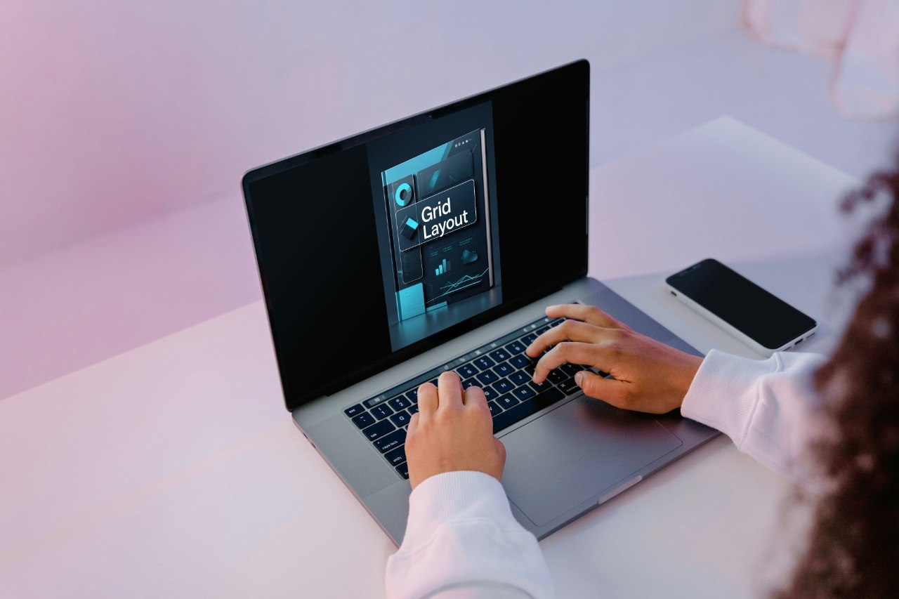 Person using a laptop with a screen displaying a 'Crystal Grid' app on a light pink background